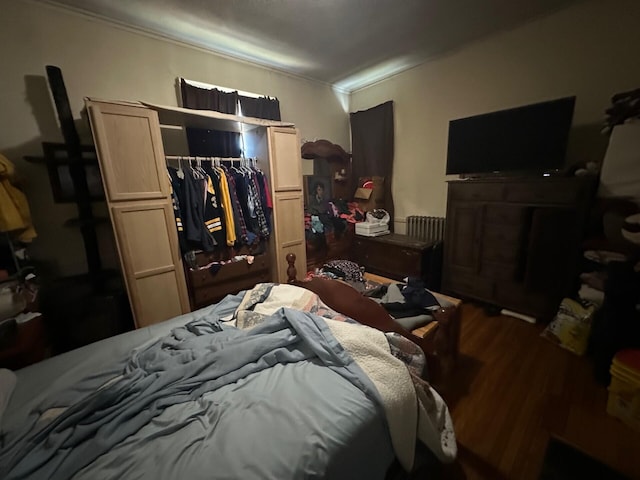 bedroom with wood-type flooring, crown molding, and a closet