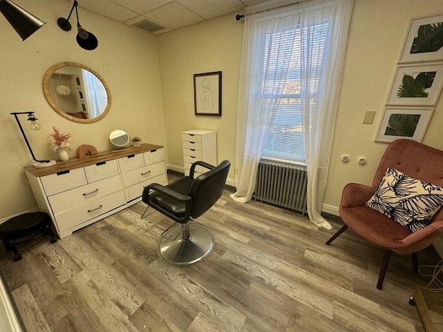 sitting room with radiator, a drop ceiling, and light wood-type flooring