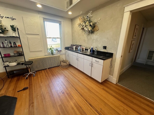 interior space with light wood-type flooring, heating unit, sink, radiator heating unit, and white cabinetry