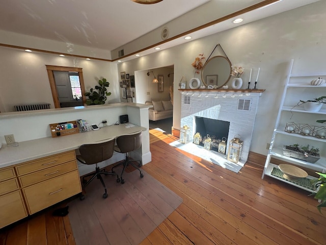 office area with light wood-type flooring, built in desk, and a brick fireplace