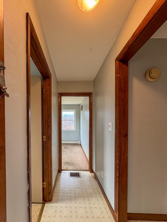 corridor with light carpet and a baseboard heating unit