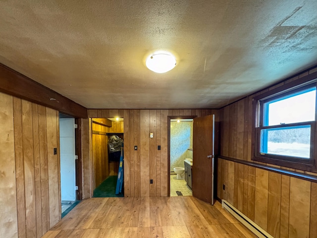 unfurnished room with a textured ceiling, wood walls, a baseboard heating unit, and light wood-type flooring