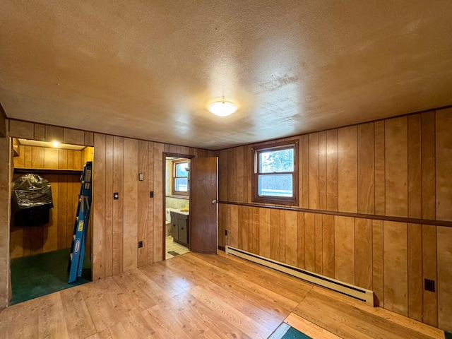 unfurnished room with light wood-type flooring, a textured ceiling, wooden walls, and a baseboard radiator