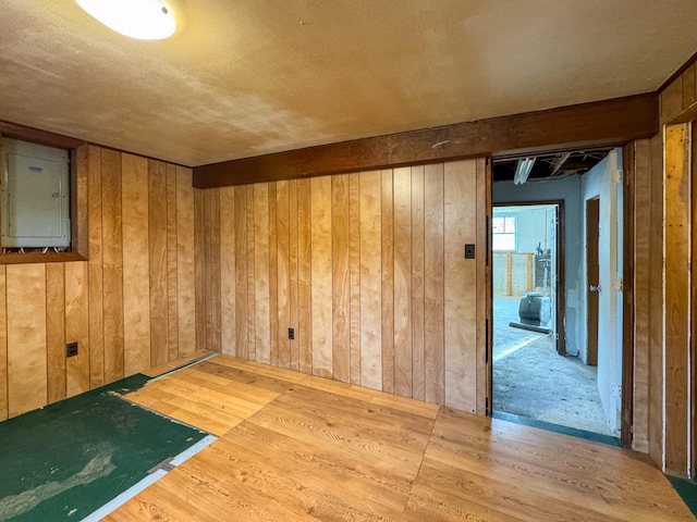 unfurnished room with electric panel, wood-type flooring, a textured ceiling, and wooden walls