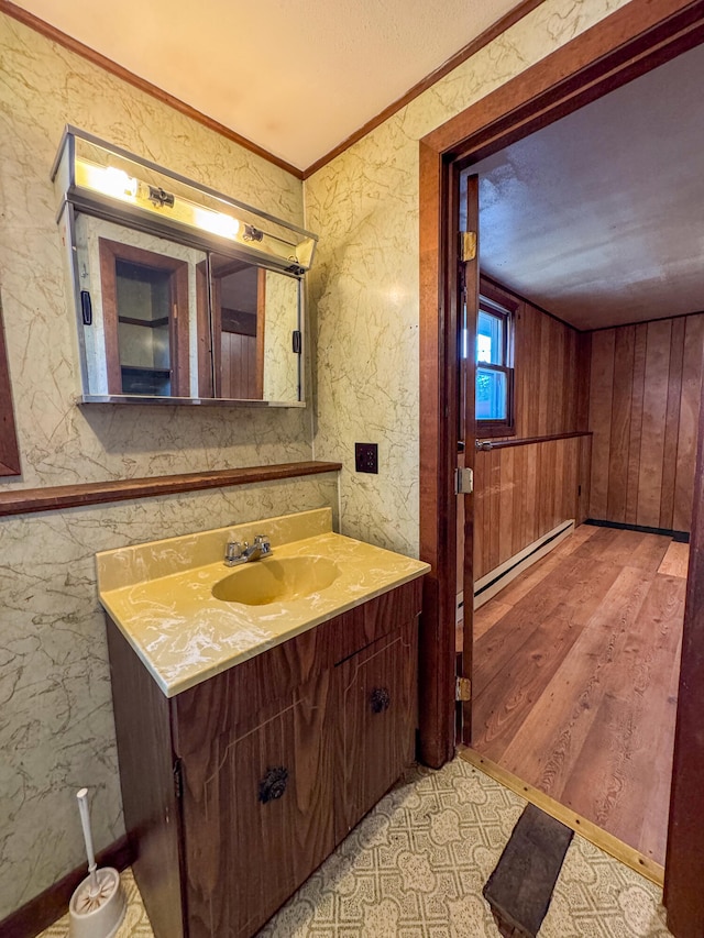 bathroom featuring vanity, a baseboard heating unit, wooden walls, ornamental molding, and wood-type flooring