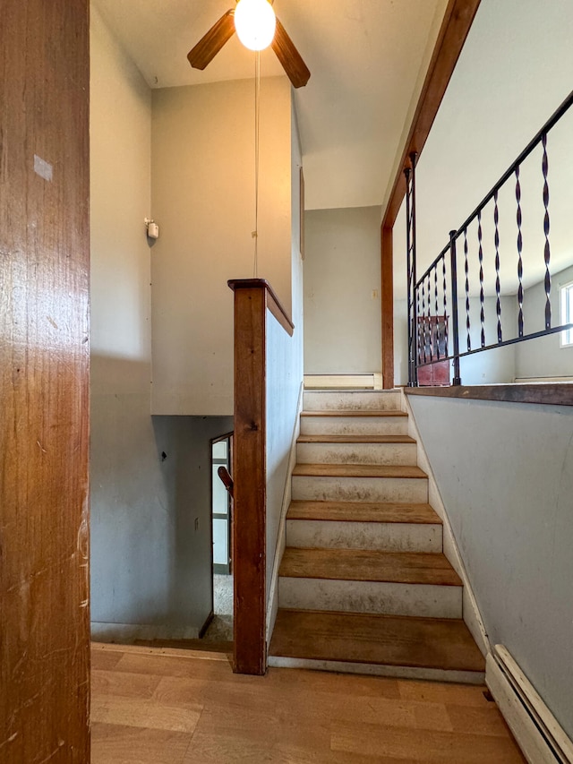 stairway featuring wood-type flooring, baseboard heating, and ceiling fan