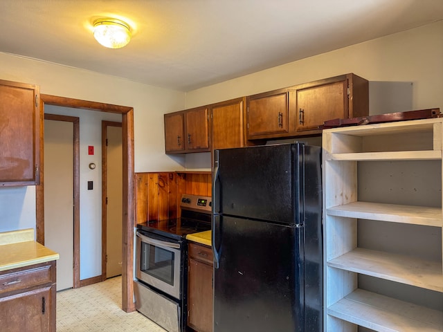 kitchen featuring black refrigerator, stainless steel range with electric cooktop, and wooden walls