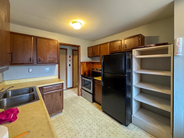 kitchen featuring black refrigerator, sink, wooden walls, and electric stove