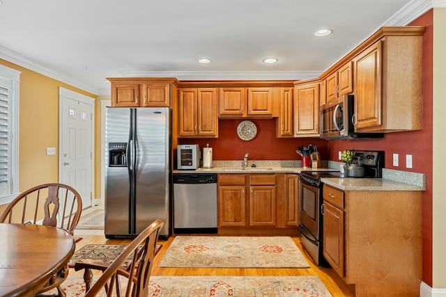 kitchen featuring sink, light stone counters, light hardwood / wood-style flooring, crown molding, and appliances with stainless steel finishes