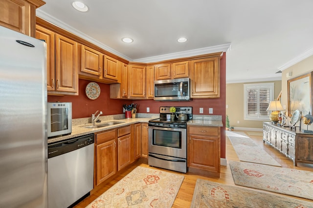 kitchen with appliances with stainless steel finishes, light stone counters, ornamental molding, sink, and light hardwood / wood-style flooring