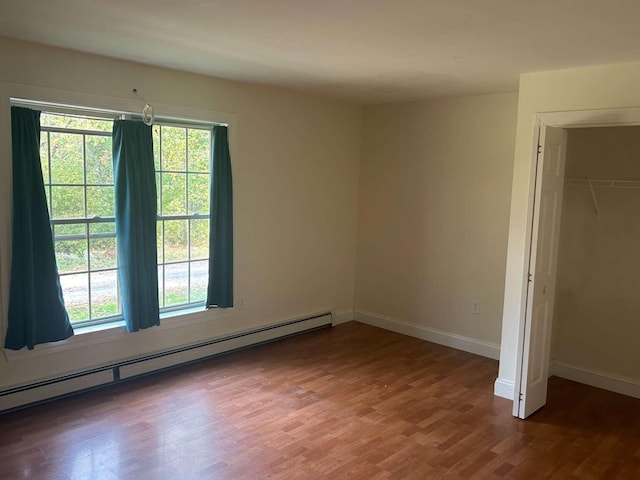 unfurnished bedroom featuring baseboard heating, a closet, and dark hardwood / wood-style floors