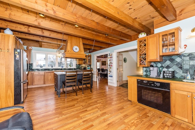 kitchen featuring pendant lighting, stainless steel fridge, light wood-type flooring, black oven, and a breakfast bar area