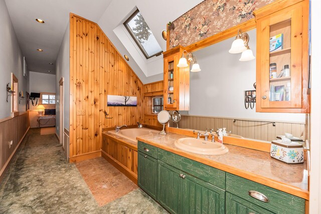 bathroom featuring vanity, wood walls, lofted ceiling with skylight, and a tub to relax in