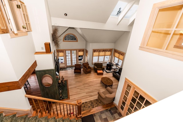 living room with a skylight, hardwood / wood-style floors, high vaulted ceiling, and french doors