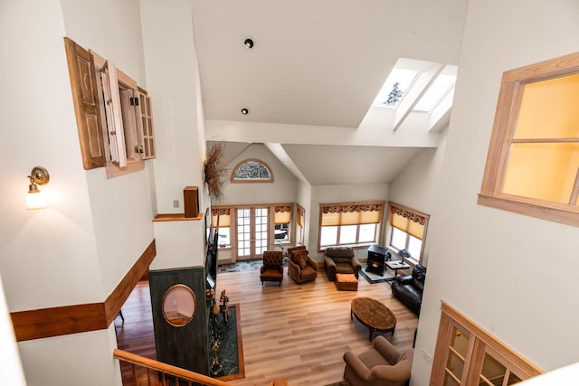 living room with a skylight, hardwood / wood-style floors, high vaulted ceiling, and french doors