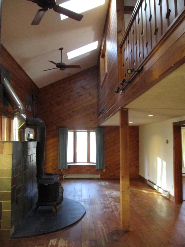 unfurnished living room with dark hardwood / wood-style flooring, a baseboard heating unit, high vaulted ceiling, a wood stove, and wood walls