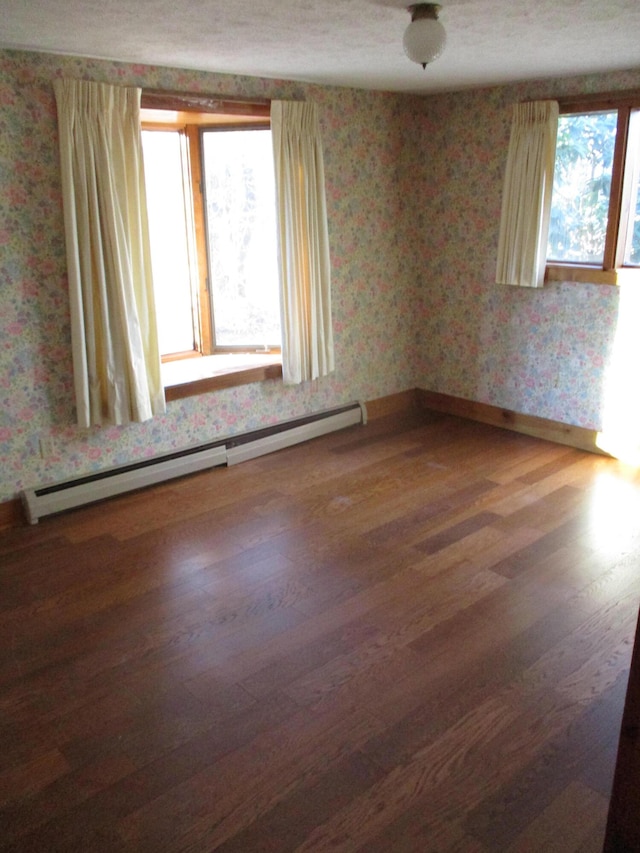 empty room featuring a healthy amount of sunlight, a baseboard radiator, and hardwood / wood-style flooring