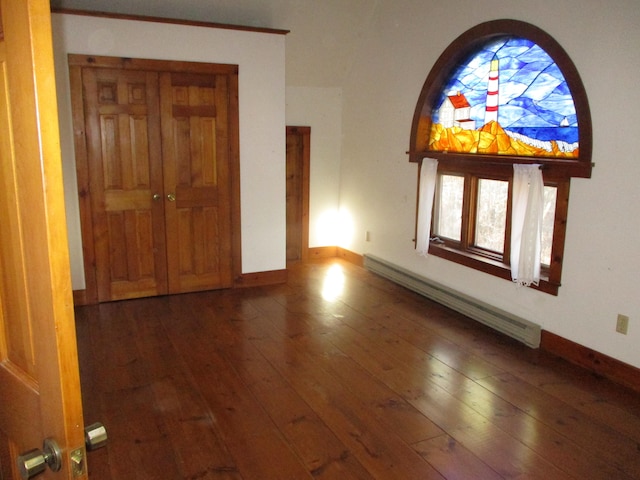 empty room with dark hardwood / wood-style flooring and a baseboard heating unit