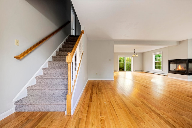 stairway featuring a multi sided fireplace, baseboard heating, an inviting chandelier, and hardwood / wood-style flooring