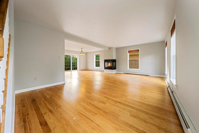 unfurnished living room featuring a notable chandelier, light wood-type flooring, and baseboard heating