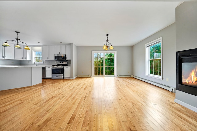 unfurnished living room with a notable chandelier, sink, light wood-type flooring, and baseboard heating