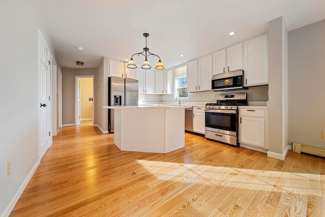 kitchen featuring appliances with stainless steel finishes, decorative light fixtures, a center island, light hardwood / wood-style floors, and white cabinetry