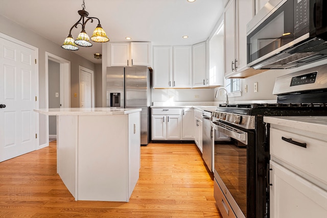 kitchen with white cabinets, appliances with stainless steel finishes, light wood-type flooring, and hanging light fixtures