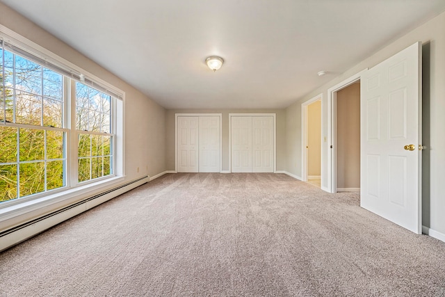 unfurnished bedroom with carpet, two closets, and baseboard heating