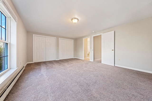 unfurnished bedroom featuring ensuite bath, carpet floors, baseboard heating, and multiple closets