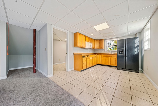 kitchen featuring a paneled ceiling, black fridge, sink, and light tile patterned floors