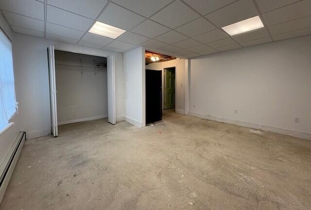 unfurnished bedroom featuring a baseboard heating unit, a paneled ceiling, and a closet