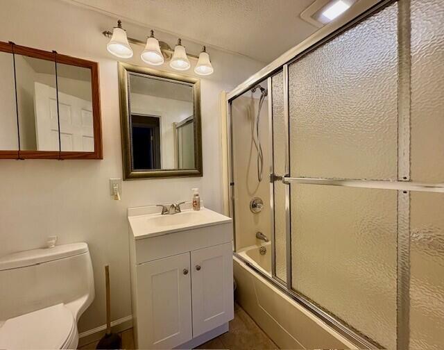 full bathroom featuring vanity, a textured ceiling, toilet, and combined bath / shower with glass door