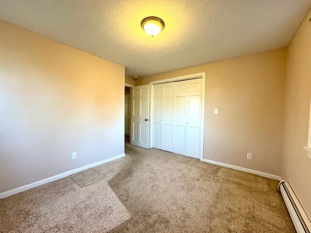 unfurnished bedroom with carpet floors, a baseboard heating unit, a textured ceiling, and a closet