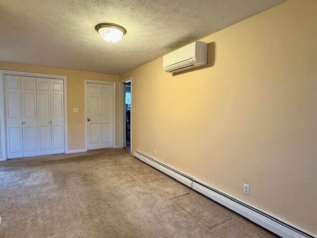 unfurnished bedroom featuring baseboard heating, light carpet, a textured ceiling, a wall unit AC, and a closet