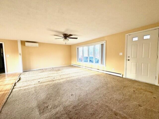 unfurnished living room featuring ceiling fan, carpet, a baseboard heating unit, and a wall unit AC