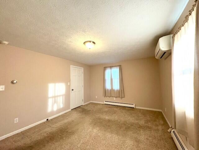 unfurnished room with a baseboard heating unit, a wall unit AC, a textured ceiling, and carpet flooring