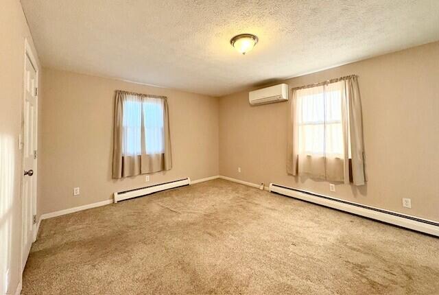 carpeted empty room with a baseboard heating unit, a wall mounted air conditioner, and a wealth of natural light