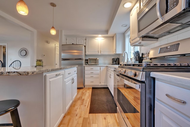 kitchen with white cabinets, hanging light fixtures, light hardwood / wood-style flooring, decorative backsplash, and appliances with stainless steel finishes