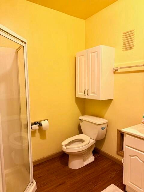 bathroom featuring vanity, hardwood / wood-style flooring, toilet, and a shower with door