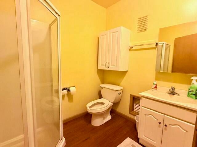 bathroom featuring hardwood / wood-style floors, vanity, toilet, and a shower with door