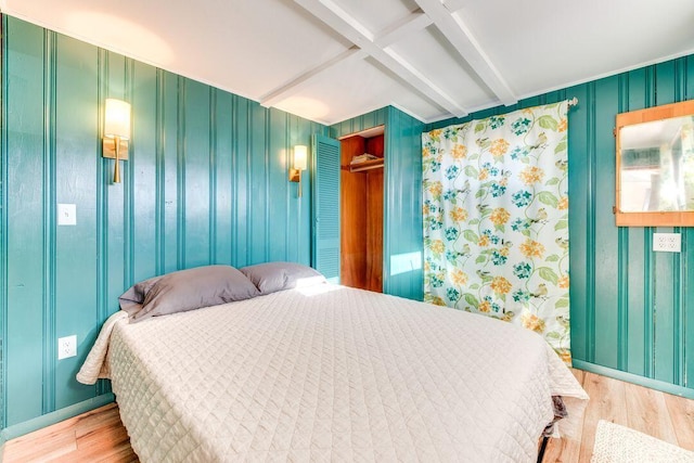 bedroom with beam ceiling, coffered ceiling, wood walls, wood-type flooring, and a closet