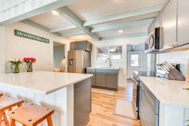 kitchen with beam ceiling, light stone countertops, stainless steel appliances, and light wood-type flooring