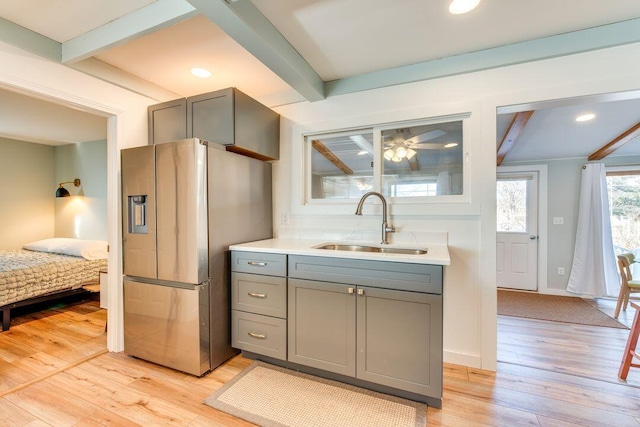 kitchen with sink, stainless steel refrigerator with ice dispenser, light hardwood / wood-style flooring, gray cabinets, and beam ceiling