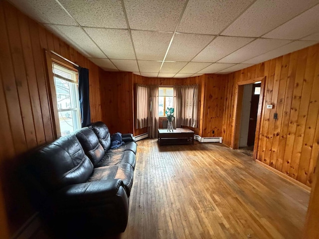 living room with a paneled ceiling, hardwood / wood-style flooring, a healthy amount of sunlight, and wood walls