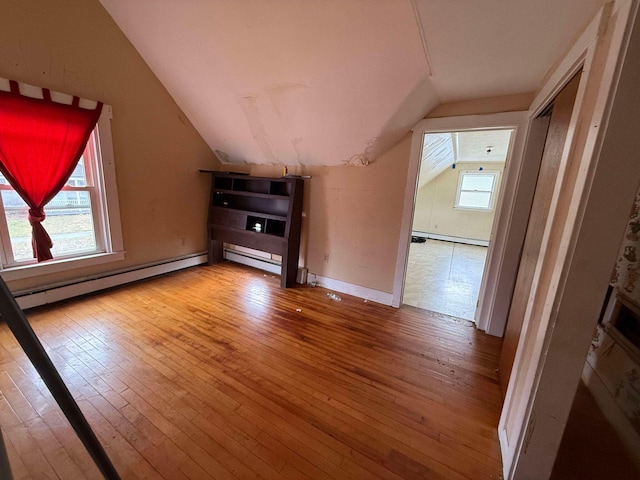 unfurnished living room featuring a baseboard heating unit, hardwood / wood-style flooring, a wealth of natural light, and lofted ceiling