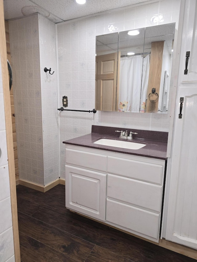 bathroom featuring vanity, a shower with shower curtain, wood finished floors, tile walls, and backsplash