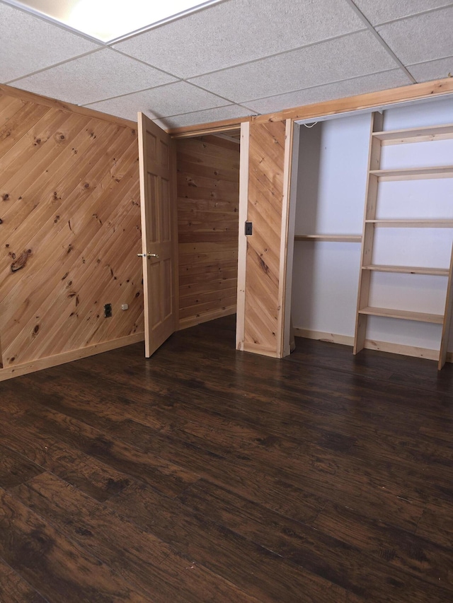 finished below grade area with wooden walls, dark wood-style floors, baseboards, and a drop ceiling