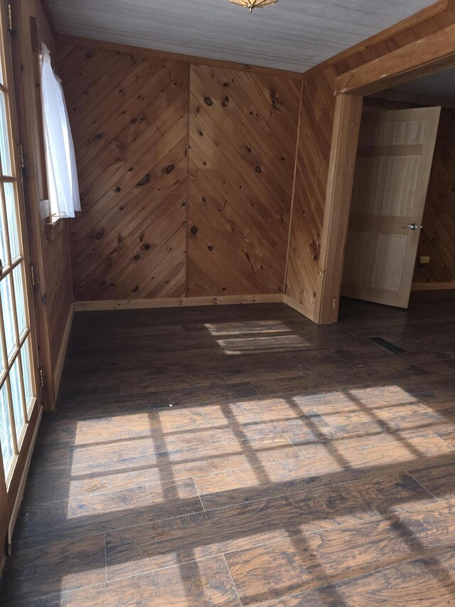 unfurnished room featuring hardwood / wood-style floors, visible vents, baseboards, and wood walls