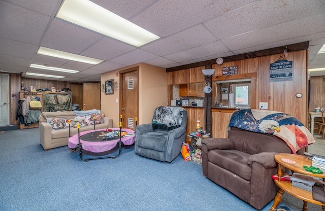 carpeted living room with a drop ceiling and wood walls
