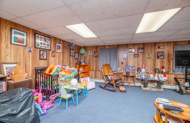 recreation room with a paneled ceiling, carpet flooring, and wood walls